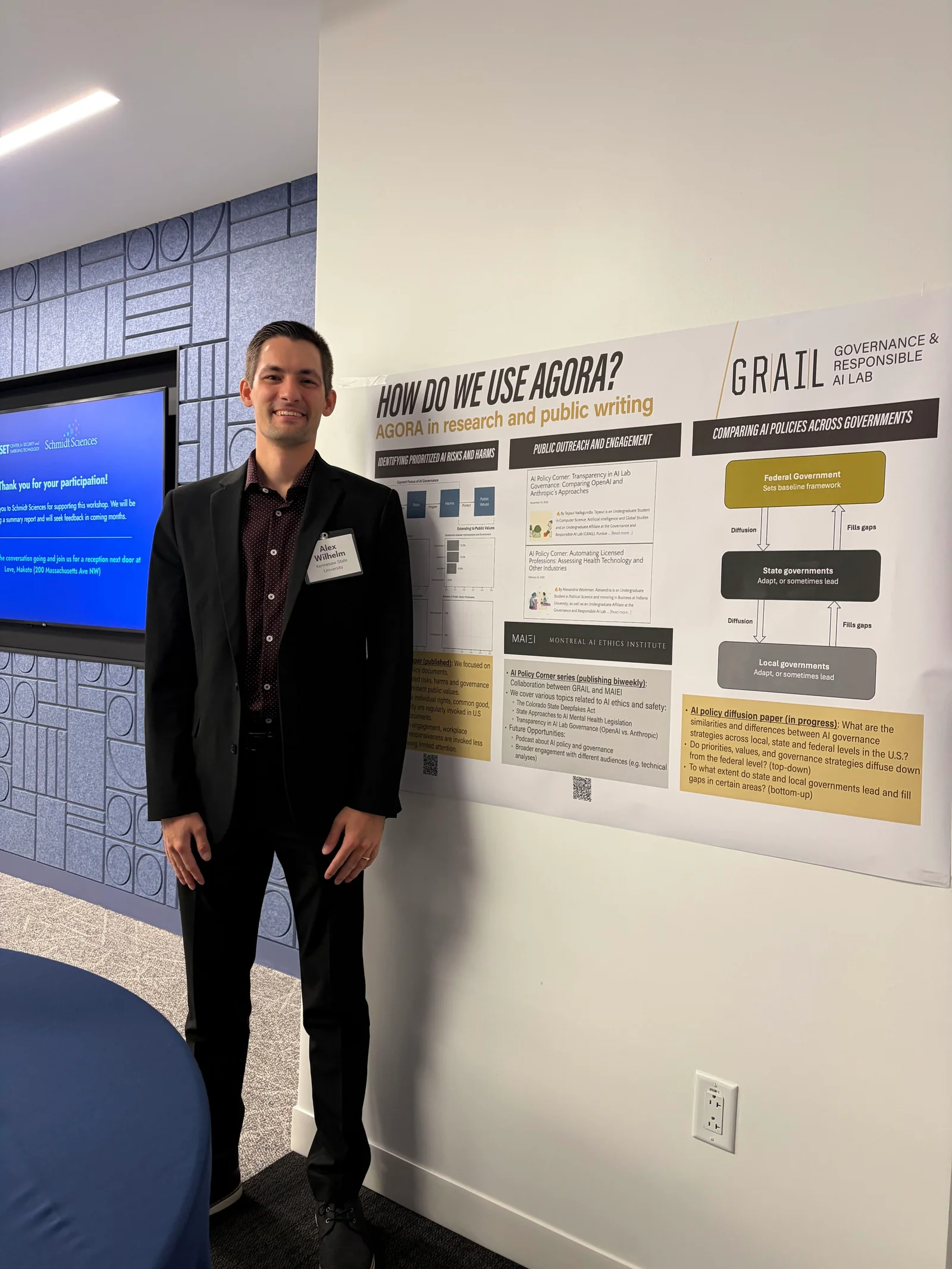 Alex Wilhelm beside a poster about AGORA research and public writing